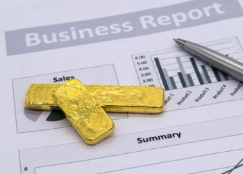 Two gold bars, symbolizing Gold Collateral, and a silver pen rest on a printed business report featuring sales charts and summary data. | GoldZeus.com