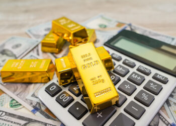 Gold bars on a calculator and scattered US dollar bills symbolize finance, investment, retirement security, and wealth management. | GoldZeus.com