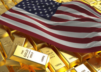 Several gold bars are stacked together, with an American flag draped over them. The gold bars are marked as "Fine Gold 999.9" and "1000g. | GoldZeus.com