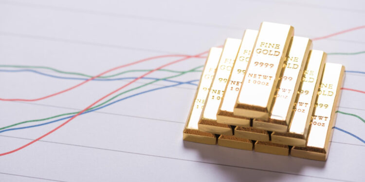A stack of gold bars is placed on a paper showing colorful financial line graphs, symbolizing wealth and investment trends. | GoldZeus.com