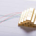 A stack of gold bars is placed on a paper showing colorful financial line graphs, symbolizing wealth and investment trends. | GoldZeus.com