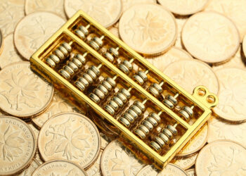 A golden abacus rests on a pile of Chinese coins with floral designs and Chinese characters. | GoldZeus.com