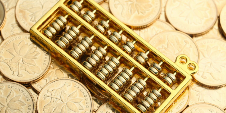 A golden abacus rests on a pile of Chinese coins with floral designs and Chinese characters. | GoldZeus.com