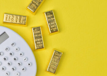 Five gold bars and a white calculator on a bright yellow background, suggesting financial calculations or investments related to gold. | GoldZeus.com