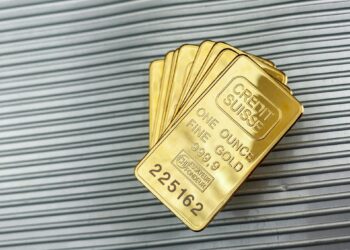 Several stacked gold bars, each labeled “CREDIT SUISSE ONE OUNCE FINE GOLD 999.9,” rest on a ribbed metallic surface. | GoldZeus.com