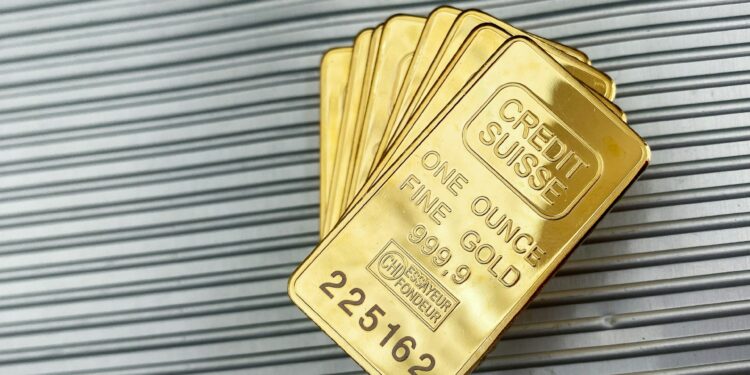 Several stacked gold bars, each labeled “CREDIT SUISSE ONE OUNCE FINE GOLD 999.9,” rest on a ribbed metallic surface. | GoldZeus.com